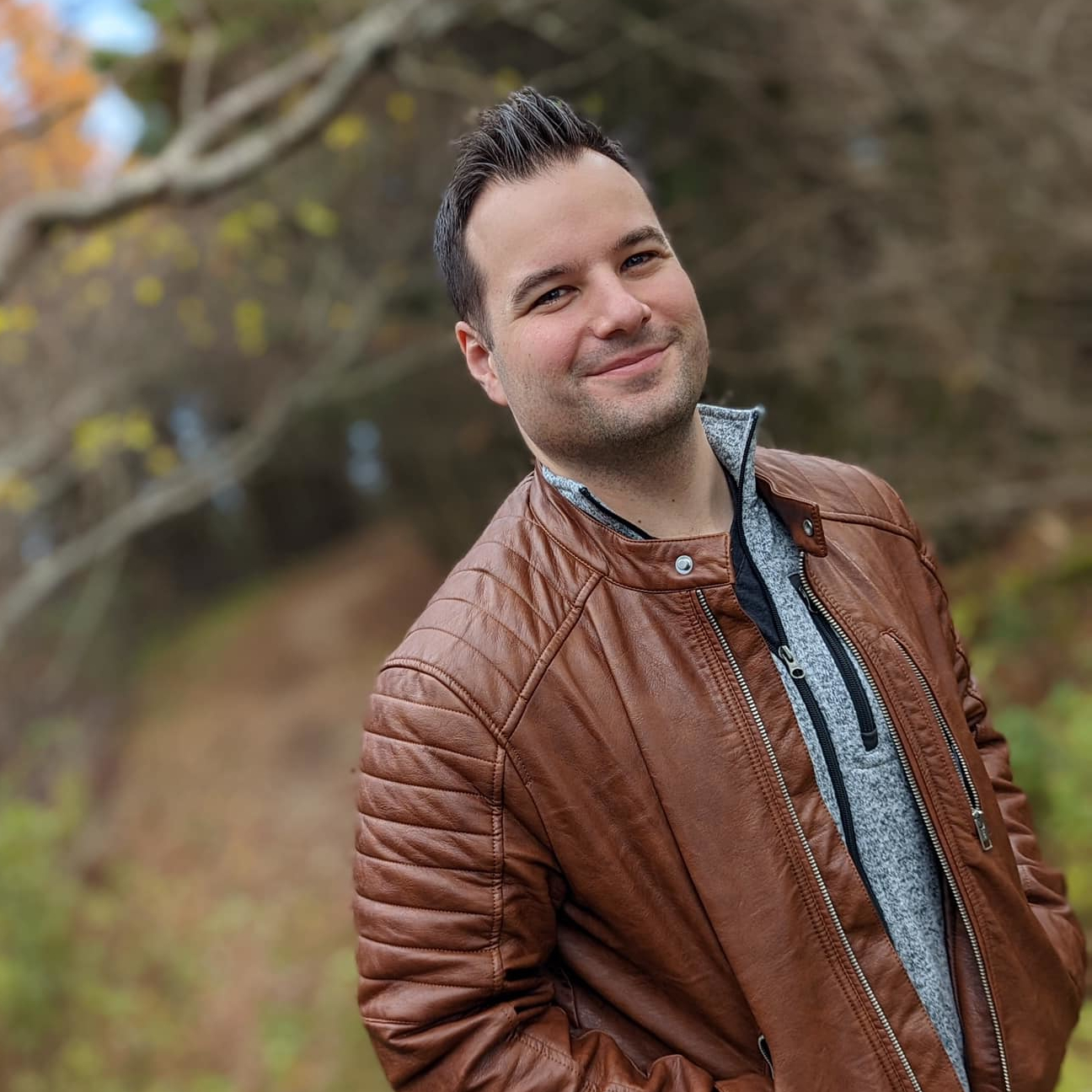 A portrait of Chris Daley standing outside and wearing a brown leather jacket while smiling.